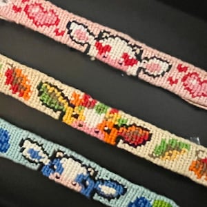 May include: Three colorful friendship bracelets with different designs. The bracelets are made with colorful embroidery floss and feature a variety of patterns, including flowers, animals, and geometric shapes.