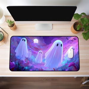 以下が含まれることがあります： ハロウィーンのシーンが描かれた長方形のマウスパッド。白い幽霊の姿が、紫と青の雲、満月、コウモリを背景に浮かんでいます。白いコンピューターマウスがパッドの上に置かれています。