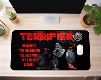 Könnte beinhalten: Schwarzes Mauspad mit dem Wort "TERRIFIER" in Rot, mit einem gruseligen Clown-Bild. Der Text auf dem Mauspads lautet: "SEIEN SIE VORSICHTIG DIESES HALLOWEEN, SIE KÖNNTEN EINEN KILLER-CLOWN SEHEN..."