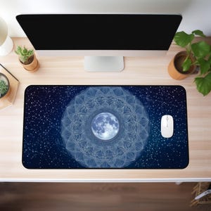 May include: A rectangular desk mat with a celestial design. The mat has a dark blue background with a detailed white mandala pattern surrounding a blue moon graphic. A white computer mouse sits on the mat.