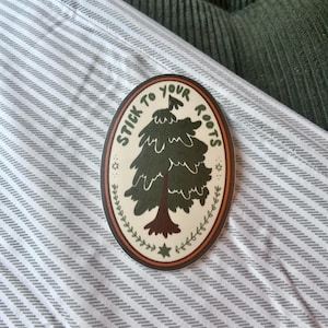 May include: A round sticker with a green tree and the text "Stick to your roots" in a white circle with a brown border.