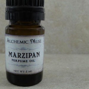 May include: A small brown glass bottle with a black cap and a white label that reads "Alchemic Muse" and "Marzipan Perfume Oil" with a net weight of 5 ml.