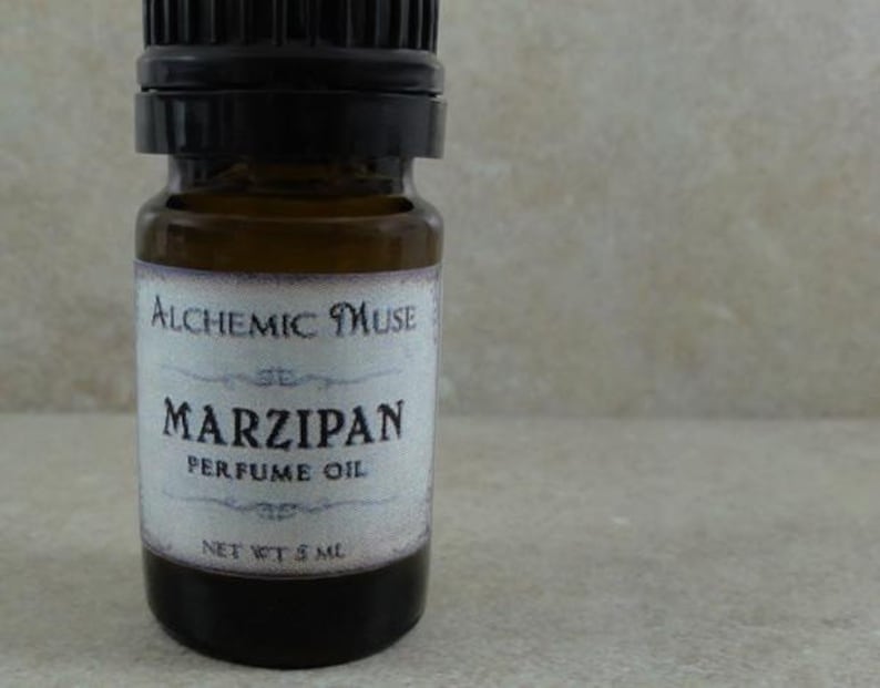 May include: A small brown glass bottle with a black cap and a white label that reads "Alchemic Muse" and "Marzipan Perfume Oil" with a net weight of 5 ml.