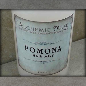 May include: A white cylindrical bottle of "Pomona Hair Mist" from "Alchemic Muse." The label is light blue with ornate script and says "Distinctive Handmade Body Care." The bottle contains 4 fl oz of product.
