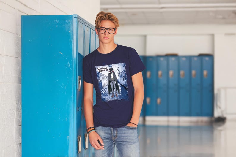 Pu&ograve; includere: Una t-shirt blu navy con una stampa grafica di una persona con un trench coat che cammina lungo un corridoio. Il testo sulla t-shirt recita "The devil is in the details".