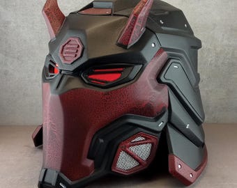May include: A black and red helmet with a textured surface and red horns. The helmet has a red visor with a black frame and a black mesh panel on the side.