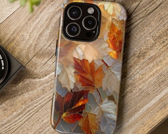 Puede incluir: Funda de teléfono inteligente con un diseño de hojas de otoño en tonos naranja, marrón y crema. La funda tiene un acabado brillante y un recorte para la cámara. La funda está sobre una superficie de madera.