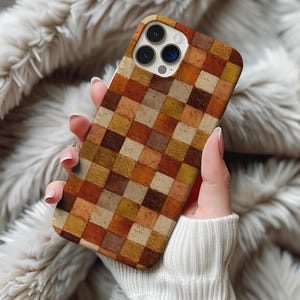 May include: A phone case with a mosaic pattern in shades of brown, orange, and beige. The case has a square grid design, with each square a different shade. The phone case is held in a person's hand.