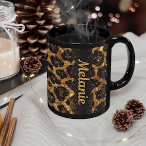 May include: A black coffee mug with a leopard print design in gold and black. The mug has the name "Melanie" printed vertically in gold. Steam rises from the mug, suggesting a hot beverage.