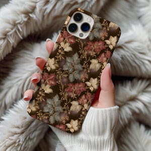 May include: A smartphone case featuring a dark brown background with a repeating pattern of autumn leaves in shades of muted red, sage green, and cream, accented by delicate golden vine-like tendrils throughout the entire surface design.