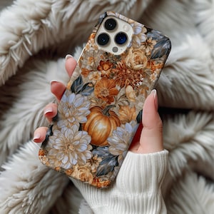 May include: A smartphone case featuring a detailed autumnal pattern with orange pumpkins, light blue and cream-colored dahlias, and various brown and gold foliage elements. The design covers the entire back of the case, including the camera cutout area.