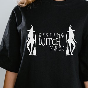 May include: Black t-shirt with a white graphic of two witches with brooms and the text "Resting Witch Face".