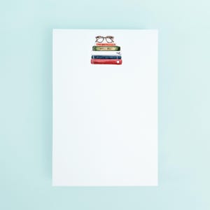 May include: A stack of five books with a pair of brown glasses on top. The books are various colors, including red, white, and green.