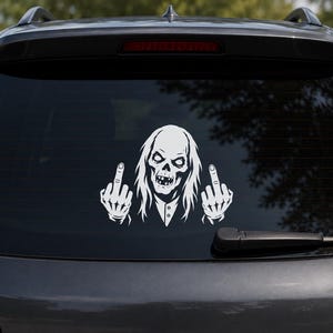 May include: A white vinyl decal applied to a car rear window, featuring a graphic illustration of a skeletal figure with long hair and a collared shirt, depicted with both hands raised and middle fingers extended in a defiant gesture.