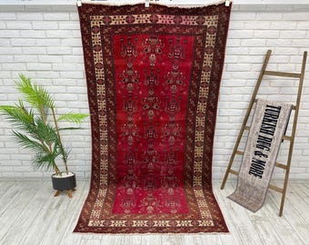 May include: A vintage Turkish rug with a red background and intricate floral patterns in shades of cream, brown, and burgundy. The rug has a border with a geometric design.