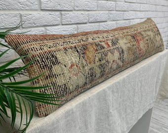 May include: Rectangular decorative pillow with a vintage rug design. The pillow features a mix of beige, red, and black colors. The pillow is placed on a white surface in front of a white brick wall.