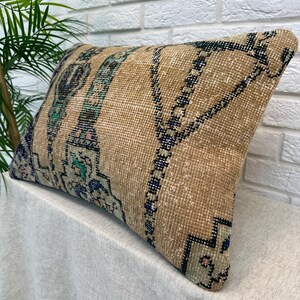 May include: A rectangular cushion with a beige background and a patterned design. The design includes teal and blue accents, and dark blue geometric shapes. The cushion is placed on a white surface.