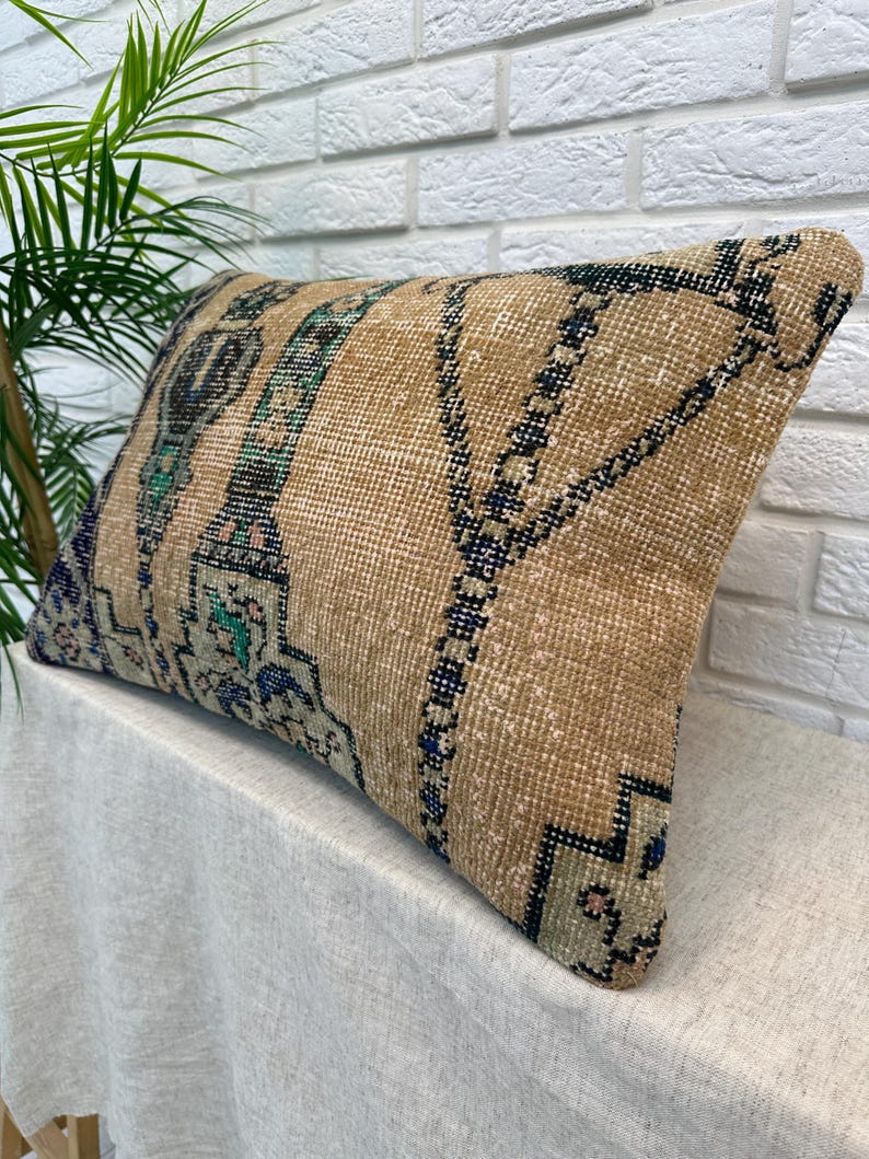 May include: A rectangular cushion with a beige background and a patterned design. The design includes teal and blue accents, and dark blue geometric shapes. The cushion is placed on a white surface.
