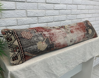 May include: A long, rectangular bolster pillow featuring a woven textile pattern in shades of deep red, charcoal gray, and cream. The fabric displays a geometric and floral motif with a distressed appearance, finished with a piped edge detail.