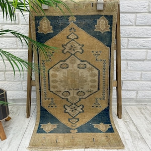 May include: A rectangular woven rug featuring a central diamond motif in tan and beige tones set against a deep blue background. The rug displays intricate geometric patterns and symmetrical floral-inspired shapes, finished with a fringed edge.