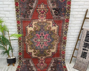 May include: A rectangular area rug featuring a central medallion design in shades of red, blue, green, and pink. The rug has a decorative border with floral motifs and a distressed texture, showcasing a complex geometric pattern throughout the surface.