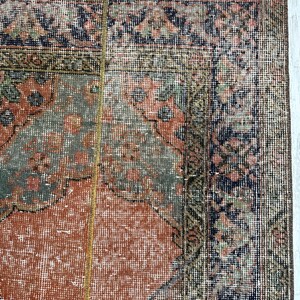 May include: A rectangular area rug featuring a central field of muted orange with intricate floral and geometric patterns in shades of sage green, navy blue, and cream. The rug has a wide, detailed border and a short, light-colored fringe edge.