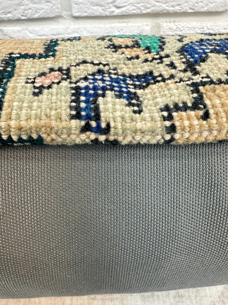 May include: Close-up of a section of a rug with a grey backing. The rug's top layer features a detailed, woven pattern in shades of blue, beige, green, and pink. The texture of the rug is visible, showcasing the intricate design.