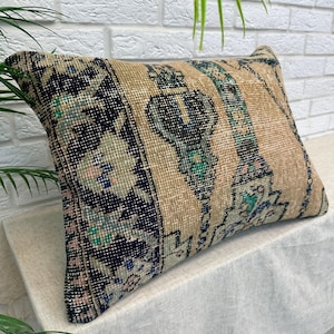 May include: Rectangular beige cushion with a vintage rug design. The cushion features a central beige panel with vertical stripes and ornate patterns in teal, navy, and pink. The ends have a navy blue and floral pattern.