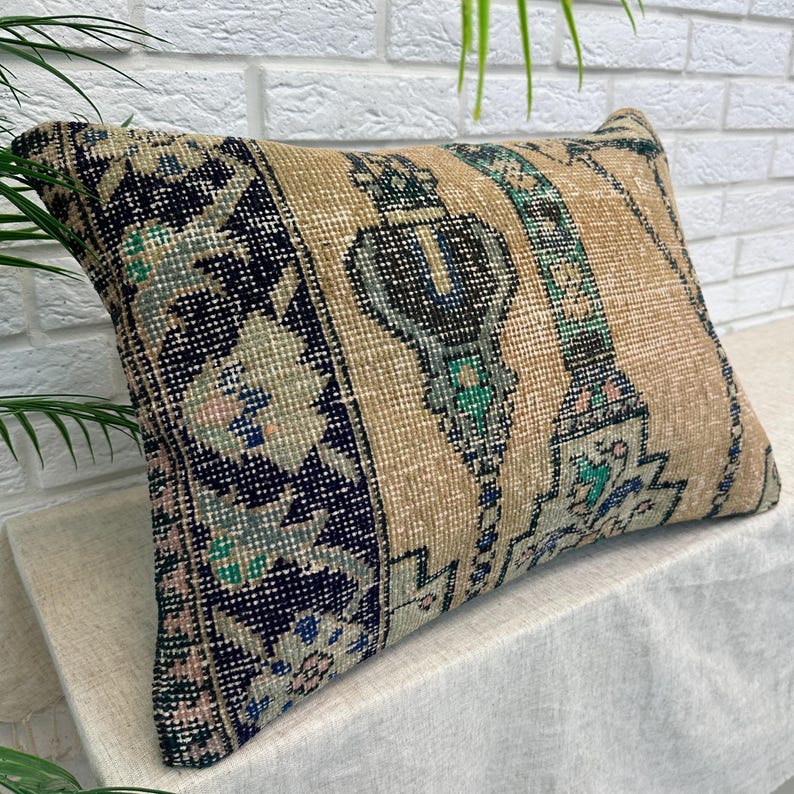 May include: Rectangular beige cushion with a vintage rug design. The cushion features a central beige panel with vertical stripes and ornate patterns in teal, navy, and pink. The ends have a navy blue and floral pattern.
