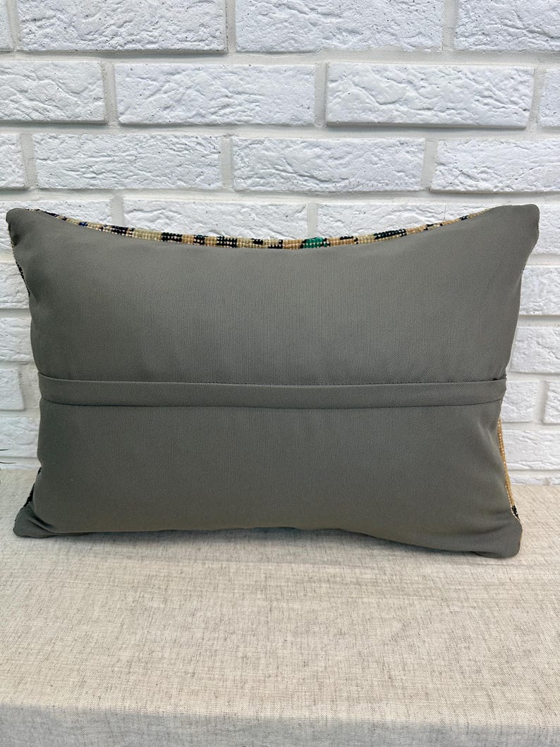 May include: A rectangular grey cushion with a patterned border. The cushion is made of a soft fabric and has a seam running across the middle. The background is a white brick wall.
