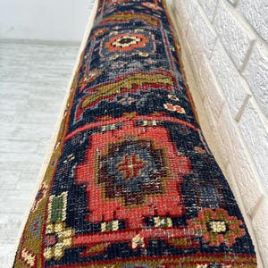 May include: A long, rectangular rug with a detailed, geometric pattern. The rug features a navy blue background with red, gold, and green accents. The design includes central medallions and borders, creating a traditional, vintage aesthetic.