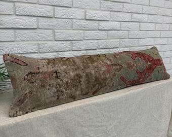 May include: A long, rectangular lumbar pillow featuring a distressed, vintage-style woven textile pattern. The fabric displays a muted color palette of faded sage green, dusty rose, and earthy brown tones in a traditional geometric motif.
