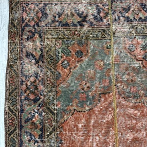 May include: A rectangular area rug featuring a complex pattern with a central field of muted orange, surrounded by borders in shades of navy blue, sage green, and dusty pink. The design includes intricate floral and geometric motifs throughout.