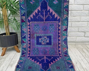 May include: A rectangular area rug featuring a central purple field with a geometric medallion, surrounded by a dark blue diamond-shaped border and a teal outer frame. The rug displays intricate patterns in shades of pink, blue, and teal.