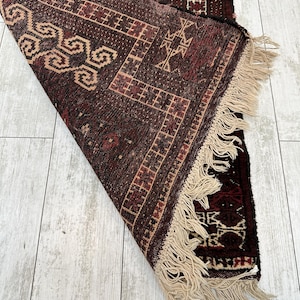 May include: A rolled-up, intricately patterned rug with a rich color palette of burgundy, brown, and beige. The rug features geometric designs and a fringe along one edge. The detailed weaving is visible.