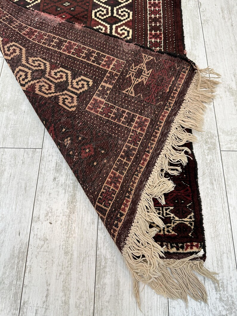 May include: A rolled-up, intricately patterned rug with a rich color palette of burgundy, brown, and beige. The rug features geometric designs and a fringe along one edge. The detailed weaving is visible.