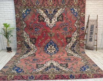 May include: A large, rectangular, vintage rug with a faded, distressed appearance. The rug features a central field of muted red with intricate floral and geometric patterns in blue, cream, and green. The border is a darker shade of red.