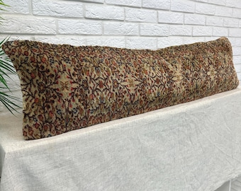 May include: A long, rectangular lumbar pillow featuring a dense, intricate floral pattern in shades of brown, tan, red, and blue. The fabric has a textured, woven appearance with a repeating botanical motif covering the entire surface.