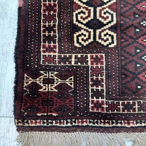 May include: Close-up of a section of a burgundy and cream-colored rug with geometric patterns. The rug has a fringe of beige tassels along the bottom edge. The design features repeating shapes and borders.