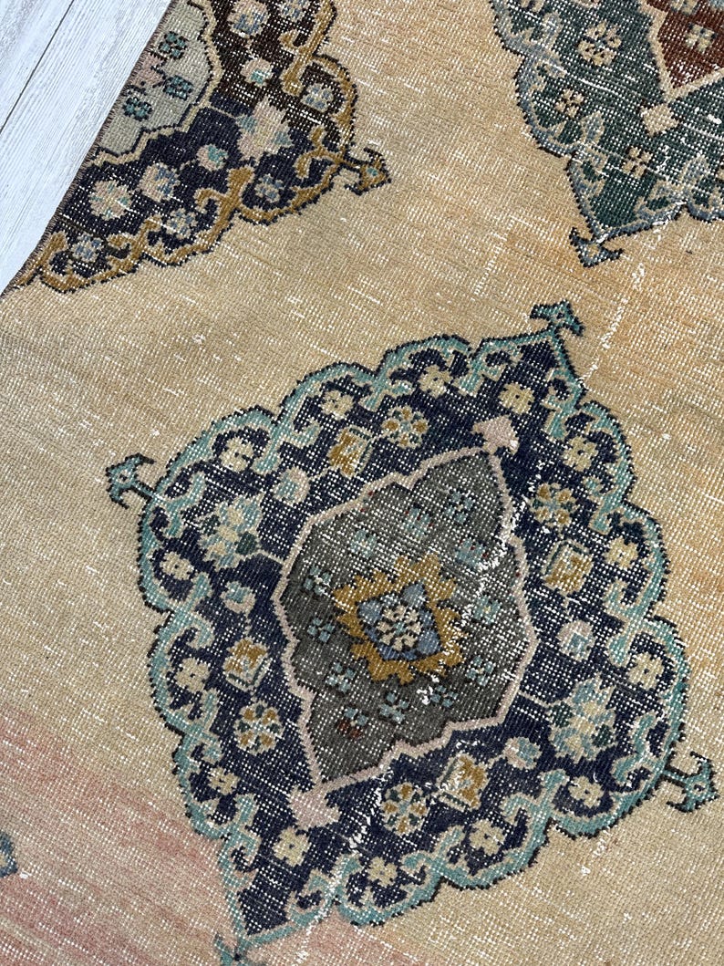 May include: A woven rug featuring a light tan base with repeating ornate medallion patterns in shades of dark blue, teal, mustard yellow, and brown. The design includes intricate geometric and floral-inspired motifs throughout.