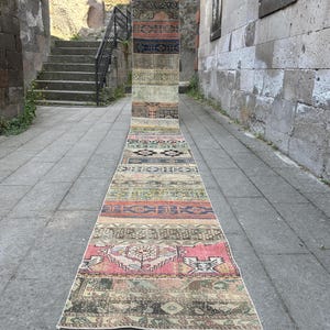 Può includere: Un tappeto a corsia lungo e stretto caratterizzato da un design patchwork composto da varie sezioni rettangolari. Il tappeto presenta una tavolozza di colori variegata che include rosa tenue, blu profondo, verde oliva e beige.