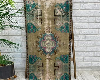 May include: A rectangular runner rug featuring a distressed, faded tan base with intricate geometric patterns in teal, dark brown, and accents of magenta. The rug has a fringed edge at the top and a symmetrical design with a central medallion motif.