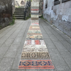 Puede incluir: Una alfombra de pasillo larga y estrecha con un diseño de patchwork compuesto por varias secciones rectangulares. La alfombra muestra una paleta de colores diversa que incluye tonos de rojo, azul, marrón, beige y gris, con patrones geométricos.