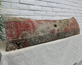 May include: A long rectangular lumbar pillow featuring a woven textile pattern in shades of muted red, beige, and dark gray. The fabric displays a distressed, weathered appearance with intricate geometric and floral motifs throughout the surface.