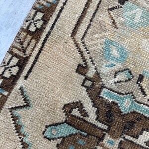 May include: Close-up of a beige and brown patterned rug with geometric and floral designs. The rug features accents of light blue and a textured surface, showcasing a traditional style.