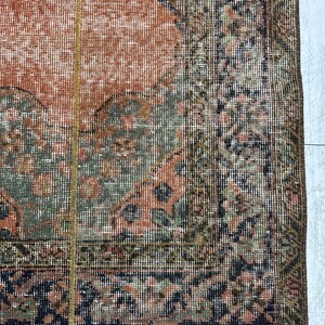 May include: A rectangular area rug featuring a distressed, faded pattern in shades of terracotta orange, sage green, and dark navy blue. The rug has a wide, intricate border with floral motifs and a central field with a geometric medallion design.