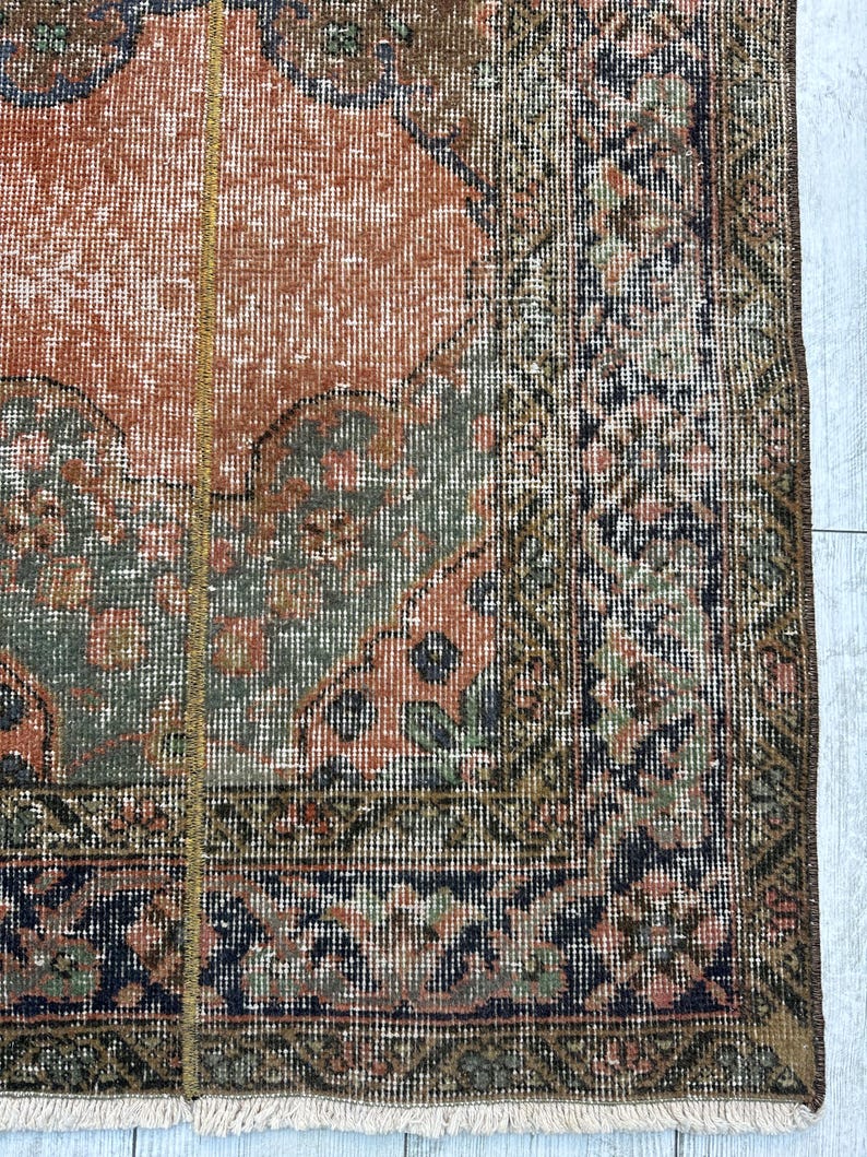May include: A rectangular area rug featuring a distressed, faded pattern in shades of terracotta orange, sage green, and dark navy blue. The rug has a wide, intricate border with floral motifs and a central field with a geometric medallion design.