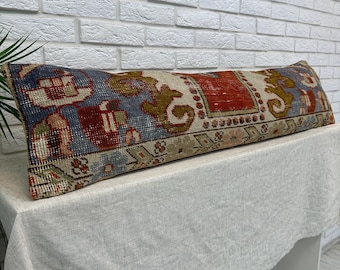 May include: A long rectangular lumbar pillow featuring a woven textile pattern in shades of deep red, muted blue, olive green, and cream. The design displays intricate geometric and floral motifs across the entire surface of the fabric cover.