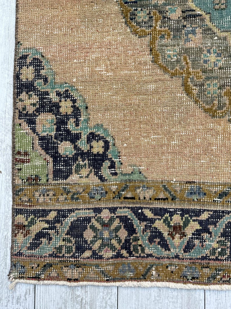 May include: A woven rug featuring a tan background with a dark blue and teal floral border. The central area displays a large, intricate medallion pattern in shades of dark blue, teal, and mustard yellow, with a fringed edge at the bottom.