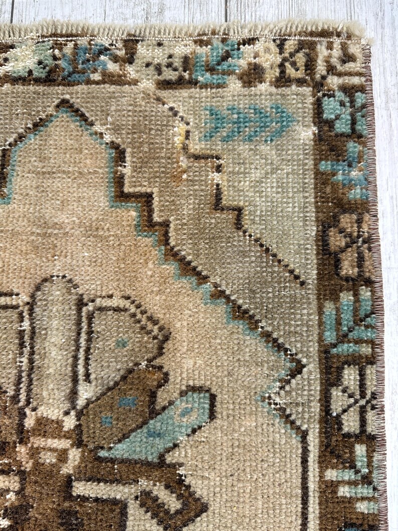 May include: Close-up of a beige and brown rug with a geometric pattern. The rug features a central design with brown and blue accents, and a border with similar colours. The rug has a distressed, vintage look.
